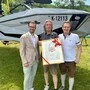 Drei Männer stehen mit einer Auszeichnung vor einem Boot