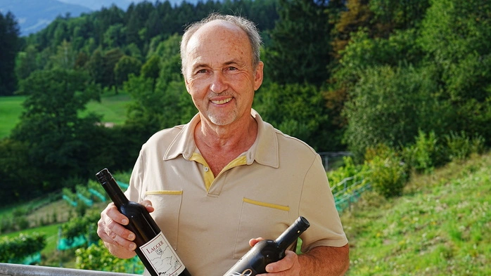 Ein Mann steht mit Weinflaschen in seinen Händen in einem Weingut