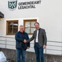 Zwei Männer schütteln sich vor einem Gemeindeamt die Hände