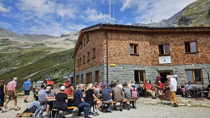 Personen sitzen auf Bänken vor einer Hütte
