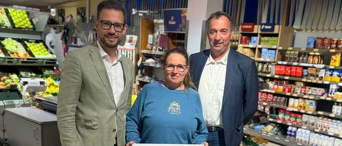 Drei Personen stehen in einem Geschäft zwischen Lebensmittelregalen