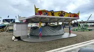 Man sieht vereinsamte Fahrgeschäfte auf einem Sandstrand bei bewölktem Wetter | Der Rummelplatz am alten Strand