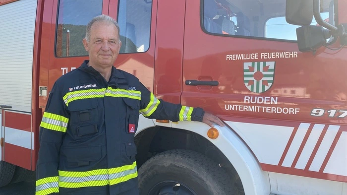 Feuerwehrmann Karl Prachoinig steht in seiner Einsatzuniform neben dem Feuerwehr-Lkw