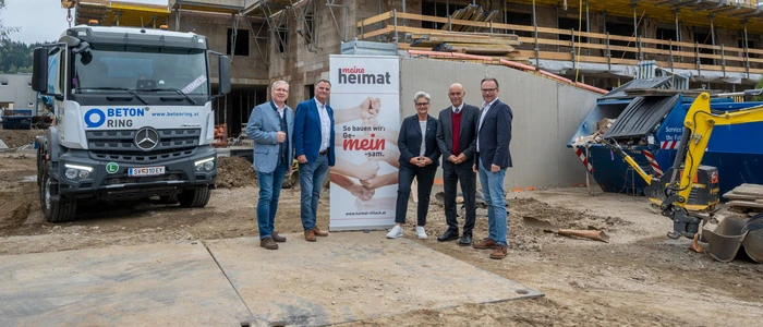 Fünf Personen stehen vor einer Baustelle und lächeln in die Kamera.