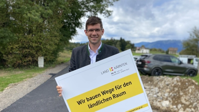 Ein Mann hält ein Schild in Händen und lächelt in die Kamera. Auf dem Schild steht: „Wir bauen Wege für den ländlichen Raum.“