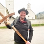Ein Mann steht vor einer Kirche in seiner Hand ein rund ein Meter langes Kreuz 