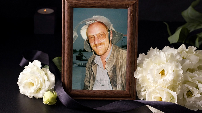 Ein umrahmtes Bild eines Mannes. Daneben liegen Trauerblumen.