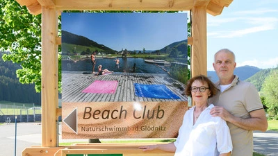 Zwei Menschen stehen neben einer Holztafel mit der Aufschrift „Beach Club“