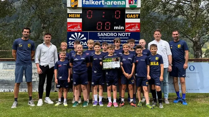 Eine Nachwuchsfußballmannschaft, flankiert von vier erwachsenen Männern. Eines der Kinder hält einen Scheck in den Händen.