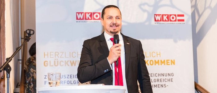 Ein Mann steht mit Mikrofon von einem Plakat der Wirtschaftskammer.
