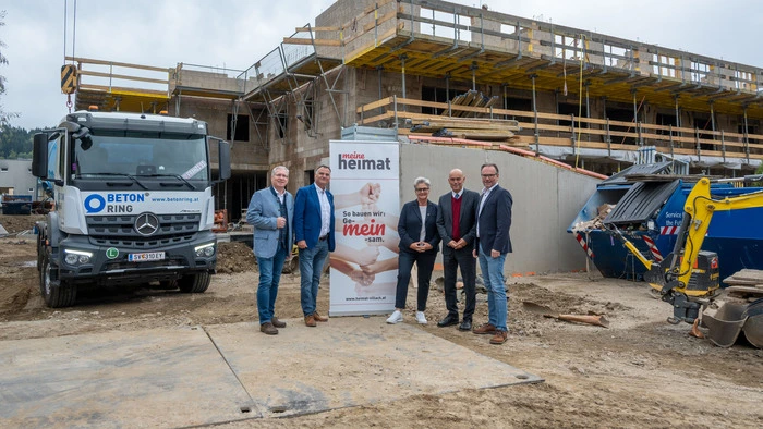 Fünf Personen stehen vor einer Baustelle und lächeln in die Kamera.