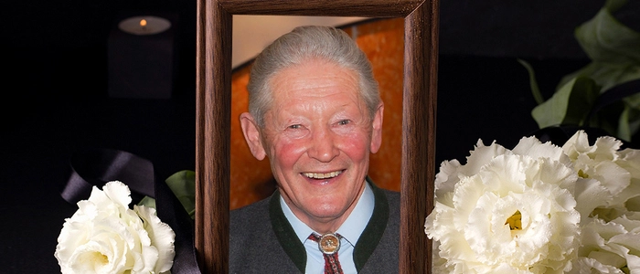 Ein gerahmtes Foto eines Mannes mit einer schwarzen Schleife, daneben weiße Rosen.