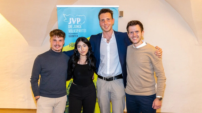 Drei junge Männer und eine junge Frau posieren für ein Foto und lächeln in die Kamera.