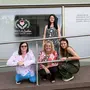Drei Frauen vor einem Second-Hand-Laden. Eine stehend, die anderen drei hockend davor.