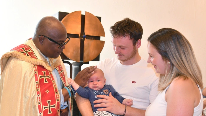 Die Eltern mit einem Priester, der ihr Kind segnet.