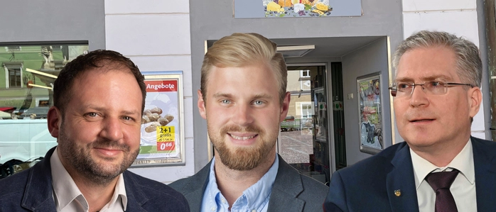 Ein Geschäft von außen. Davor die drei Köpfe der Politiker 