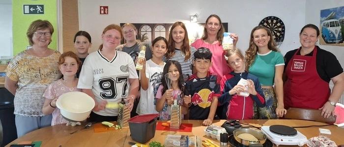 Eine Gruppe von Kindern posiert neben ein paar Erwachsenen für ein Foto. Sie nehmen an einem Kochkurs teil.
