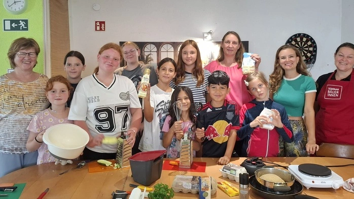 Eine Gruppe von Kindern posiert neben ein paar Erwachsenen für ein Foto. Sie nehmen an einem Kochkurs teil.