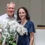 Ein Mann und eine Frau lächeln in die Kamera. Eine Orchidee steht vor ihnen.