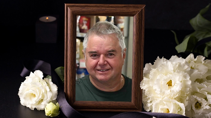 Ein umrahmtes Bild von einem Mann. Daneben sind Blumen zu sehen.