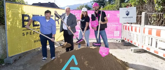 Drei Männer und eine Frau führen einen Spatenstich durch und lächeln in die Kamera.