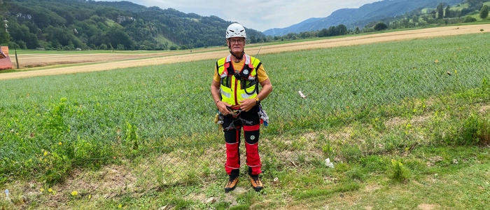 Ein Mann steht mit einer Bergrettungsausrüstung vor einem Maisfeld.
