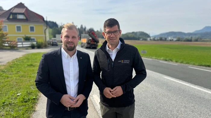 Zwei Männer stehen an einer Straße und lächeln in die Kamera.
