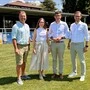 Drei Männer und eine Frau stehen auf einem Sportplatz und lächeln bei Sonnenschein in die Kamera.
