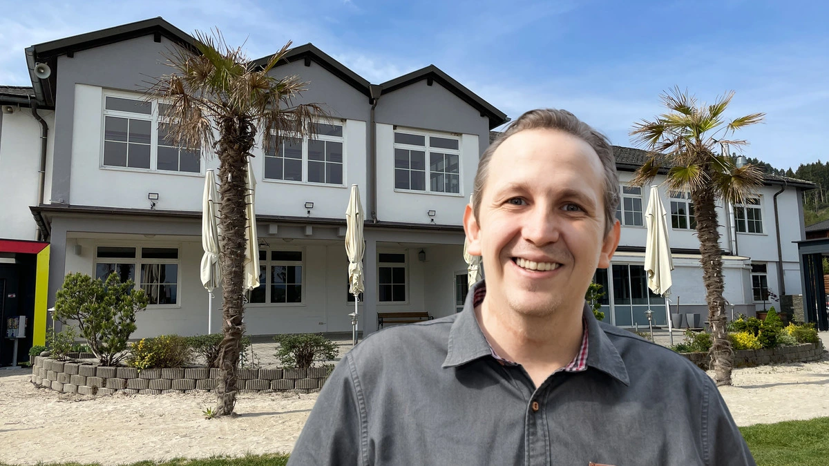 Ein Mann ist auf einer Fotomontage vor einem Gebäude abgebildet. 