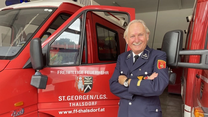 Ein Mann steht mit verschränkten Händen und Uniform vor einem Feuerwehrauto 
