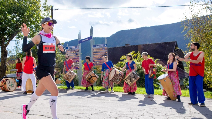 Eine Frau läuft einen Marathon. Im Hintergrund sieht man Menschen mit Trommeln, die die Athletin anfeuern.