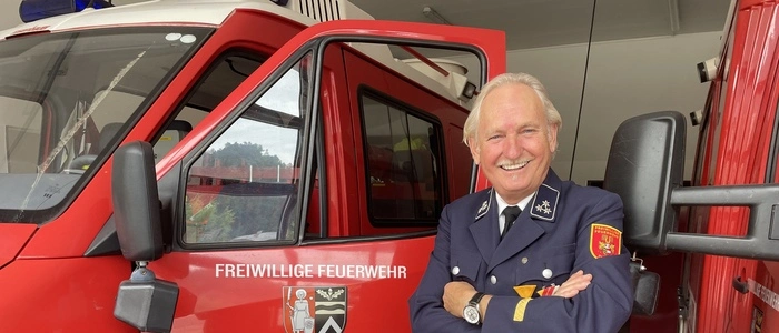 Ein Mann steht mit verschränkten Händen und Uniform vor einem Feuerwehrauto