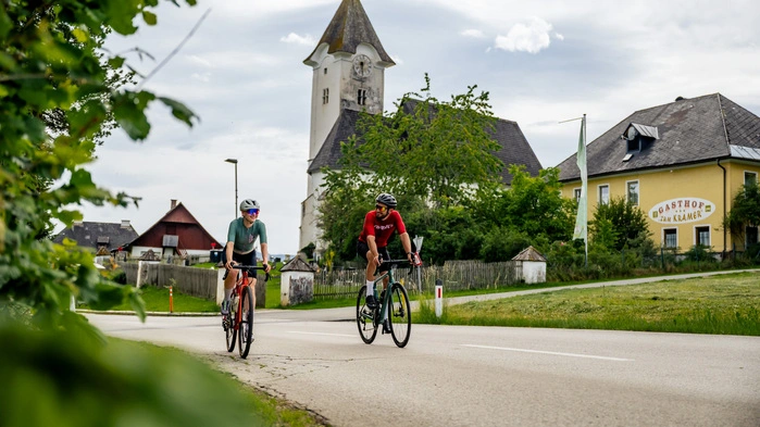 Eine Radfahrerin und ein Radfahrer fahren durch eine Ortschaft.