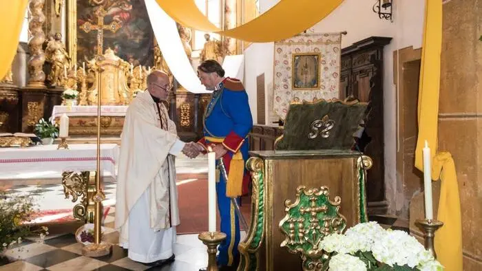 Ein Pfarrer und ein Bürgermeister stehen in der Kirche und geben sich die Hand.