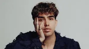 Der Künstler sitzt in einem weißen Raum und stützt sein Gesicht mit seiner rechten Hand  | Christof Schratt würde gerne für Österreich beim ESC antreten 