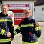 Zwei Männer in Feuerwehruniform reichen sich die Hände. Sie stehen vor einem Rüsthaus 