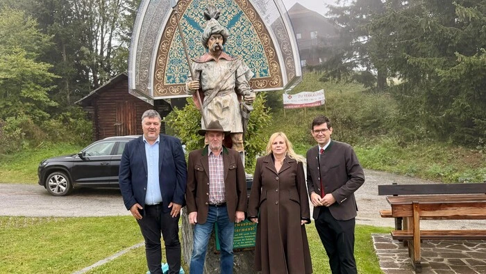 Drei Männer und eine Frau stehen vor einer Skulptur und lächeln in die Kamera.