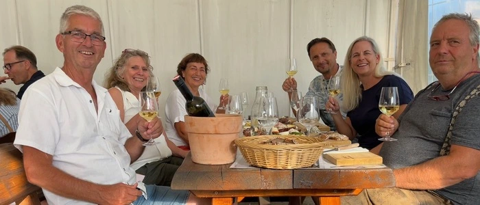 Eine Runde von Menschen sitzt an einem Tisch, alle genießen ein Glas Wein.