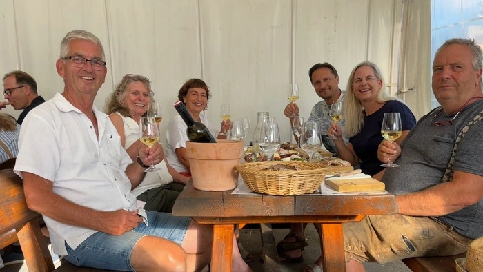 Eine Runde von Menschen sitzt an einem Tisch, alle genießen ein Glas Wein.
