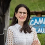 Eine Frau steht vor einem Schild und lächelt in die Kamera.