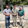 Drei Männer stehen vor einem Kriegerdenkmal und lächeln in die Kamera.