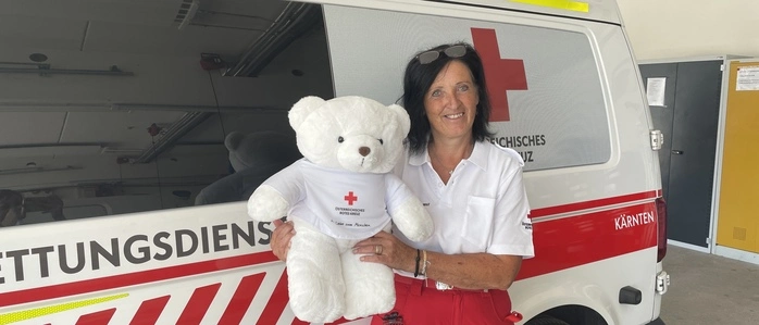 Eine Frau steht vor einem Rettungsauto und hält einen Teddybären in der Hand 