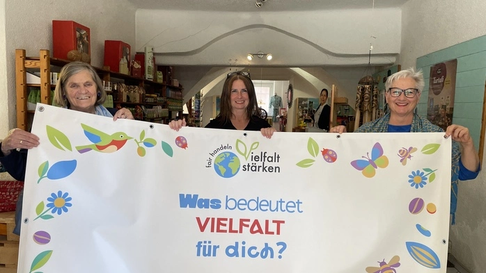 Drei Frauen stehen hinter einem Transparent. Zu lesen ist „Was bedeutet Vielfalt für dich?“