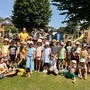 Einige Kinder sowie ein paar Erwachsene stehen vor einem Spielplatz und lächeln in die Kamera.