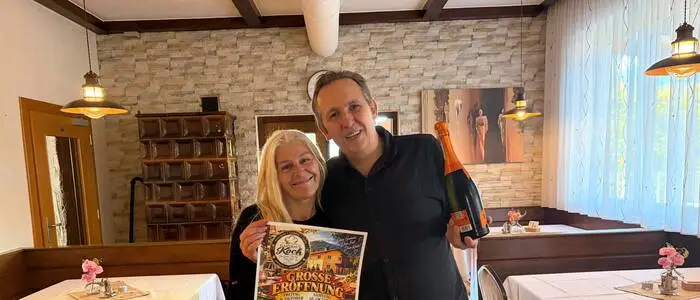 Eine Frau und ein Mann lächeln in die Kamera. Die Frau hält ein Plakat in der Hand.