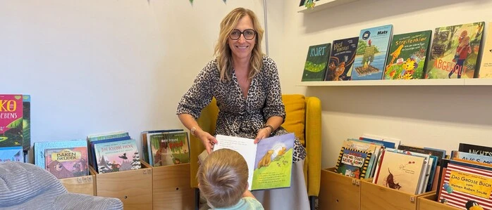 Eine Frau hält ein Buch in der Hand. Vor ihr ein Kind, das die Seiten anschaut