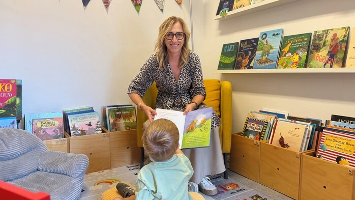 Eine Frau hält ein Buch in der Hand. Vor ihr ein Kind, das die Seiten anschaut