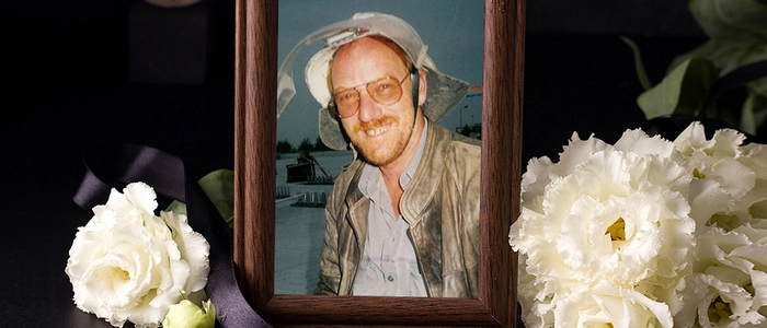 Ein umrahmtes Bild eines Mannes. Daneben liegen Trauerblumen.