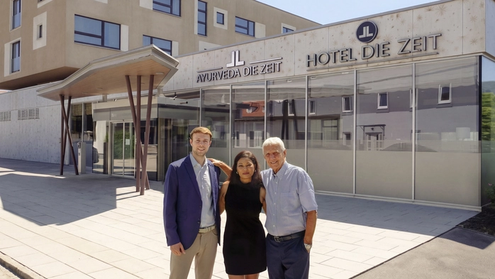 Drei Menschen stehen vor einem Hotel und schauen in die Kamera