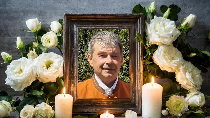 Ein gerahmtes Foto. Umrahmt von Blumen und Kerzen. 